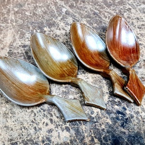 Puede incluir: Cuatro cucharas de madera con cuencos ovalados y mangos en forma de diamante. Las cucharas tienen un acabado de veta de madera natural, con variaciones de color de marrón claro a marrón oscuro. Las cucharas están dispuestas sobre una superficie marrón texturizada.