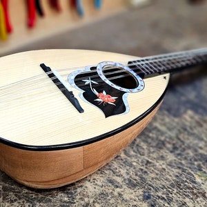 Pode incluir: Um bandolim de madeira com um desenho floral preto e branco na caixa de resson&acirc;ncia. O bandolim tem um acabamento em madeira clara e uma tarraxa de afina&ccedil;&atilde;o prateada.