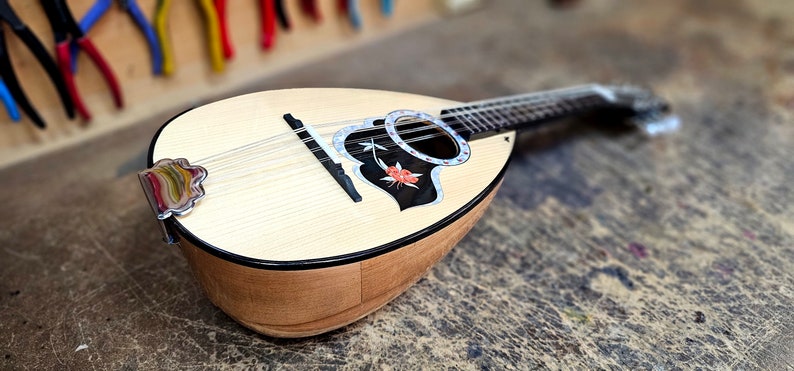 Pode incluir: Um bandolim de madeira com um desenho floral preto e branco na caixa de resson&acirc;ncia. O bandolim tem um acabamento em madeira clara e uma tarraxa de afina&ccedil;&atilde;o prateada.