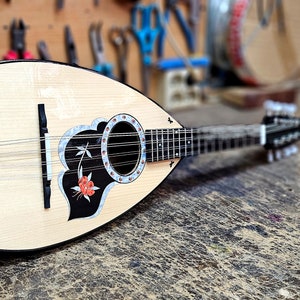 Pode incluir: Um ala&uacute;de de madeira com um desenho floral preto e branco na caixa de resson&acirc;ncia. O ala&uacute;de tem um bra&ccedil;o preto e pinos de afina&ccedil;&atilde;o prateados.