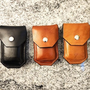 May include: Three leather pouches in black, brown, and tan. Each pouch has a flap closure secured by a silver snap. The pouches are rectangular with a slightly tapered bottom.