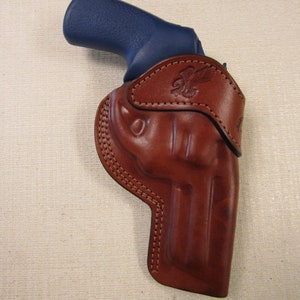 May include: A brown leather holster with a stitched design and a blue gun inside.