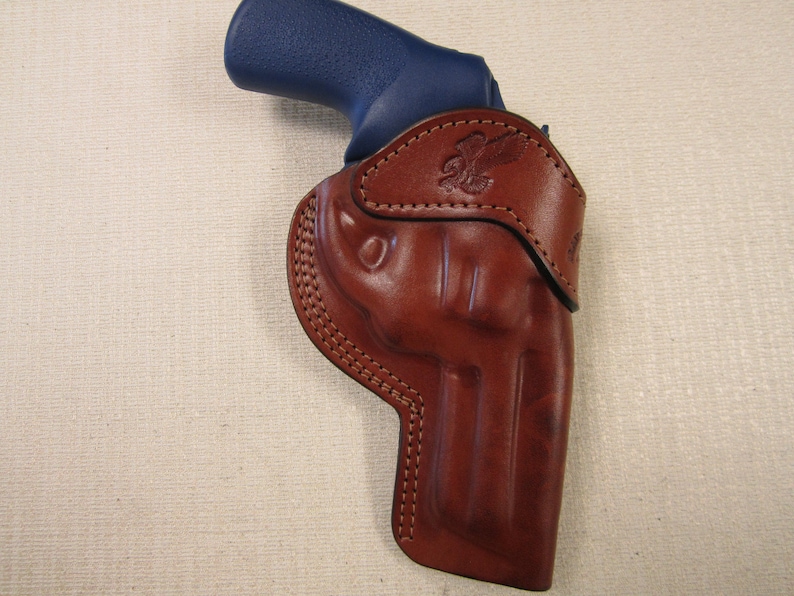 May include: A brown leather holster with a stitched design and a blue gun inside.