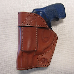 May include: A brown leather holster with a stitched design and an eagle emblem. The holster is designed to hold a blue handgun.