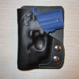 May include: A black leather holster with a snap closure and an eagle logo. A blue handgun is inside the holster.