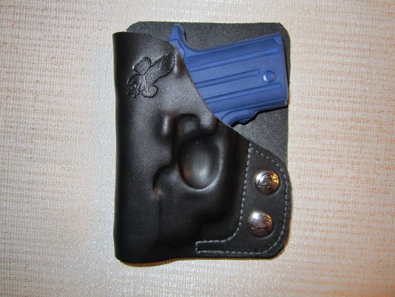 May include: A black leather holster with a snap closure and an eagle logo. A blue handgun is inside the holster.