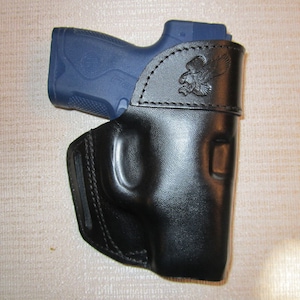 May include: A black leather holster with an eagle design. The holster is designed to hold a small, blue handgun.