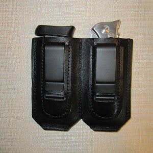 May include: Two black leather holsters with a clip on the back. Each holster has a silver metal object inside.