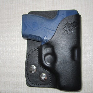 May include: A black leather holster with a blue handgun inside. The holster has a small eagle design on the side.