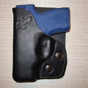 May include: A black leather holster with a snap closure and a bird design. A blue handgun is in the holster.