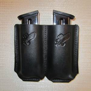 May include: Two black leather magazine holders with an eagle design. Each holder has a silver magazine inside.