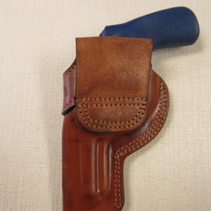 May include: A brown leather holster with a stitched design. The holster is designed to hold a firearm with a blue handle.