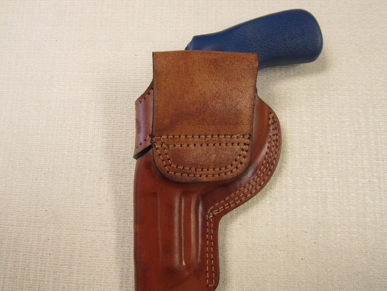 May include: A brown leather holster with a stitched design. The holster is designed to hold a firearm with a blue handle.