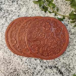 May include: Four brown leather coasters with a floral embossed design.
