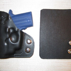 May include: A black leather holster with a blue gun inside. The holster has two silver snaps on the side. There is a black leather flap with two silver snaps on the right side of the image.