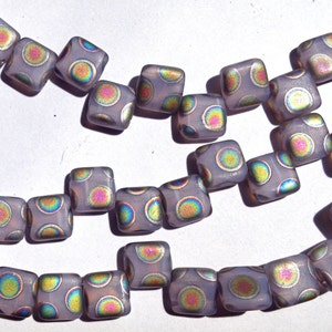 May include: Strands of square, lavender-colored beads with iridescent, multi-colored dot patterns. The beads are strung together, showcasing a repeating design. These beads are suitable for jewelry making.
