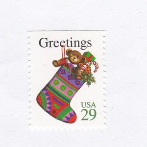May include: A vintage Christmas postage stamp featuring a red and green stocking with a teddy bear inside. The stamp says "Greetings" and "USA 29".