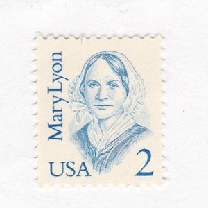 May include: A blue and white postage stamp featuring a portrait of Mary Lyon, with the text "Mary Lyon" and "USA" printed on the stamp. The stamp has a denomination of "2".