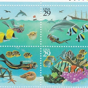 May include: Four US postage stamps featuring underwater scenes. The top left stamp shows a scuba diver, two yellow fish, and a pufferfish. The top right stamp shows a dolphin, a sailboat, and three black and white fish. The bottom left stamp shows a scuba diver, a nautilus shell, a starfish, and three yellow and black fish. The bottom right stamp shows a coral reef with a variety of colorful fish.