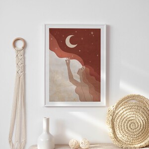 May include: A framed illustration of a woman with flowing hair reaching up to touch a crescent moon in a starry night sky. The background is a gradient of red and brown with white clouds.