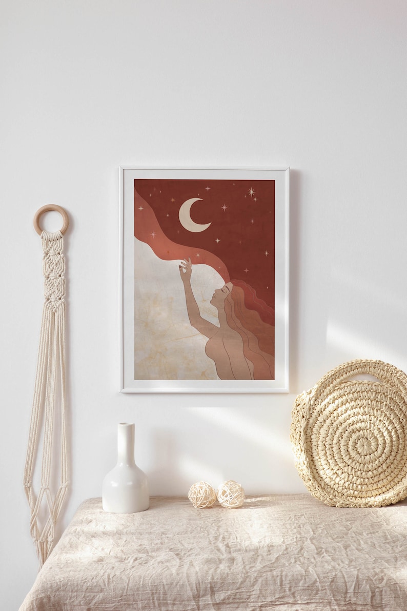 May include: A framed illustration of a woman with flowing hair reaching up to touch a crescent moon in a starry night sky. The background is a gradient of red and brown with white clouds.