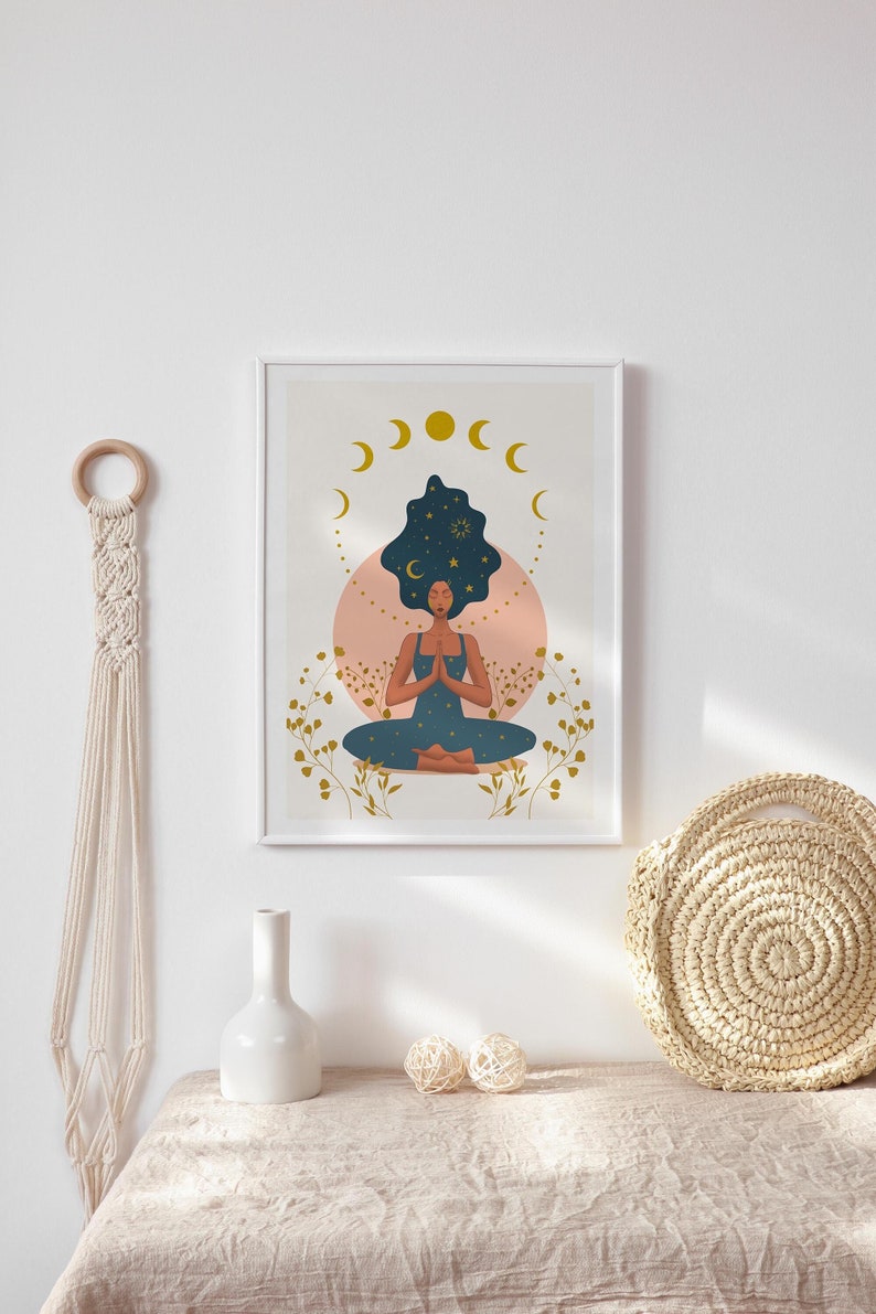 May include: A framed print of a woman meditating with a starry sky in her hair. The print is surrounded by a white frame and features a pink and white background with gold accents.
