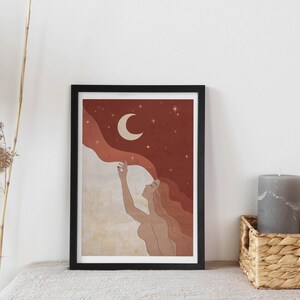May include: A framed print of a woman with long red hair reaching up towards a crescent moon in a starry night sky. The background is a gradient of red, orange, and white.