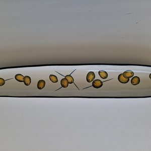 May include: A white ceramic serving dish with a black rim, featuring a design of green olives with brown pits, scattered across the surface.