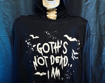 Könnte beinhalten: Ein Skelett trägt einen schwarzen Kapuzenpullover mit dem weißen Schriftzug "Goth's Not Dead, I Am" und Fledermaus-Grafiken. Der Hintergrund ist ein dunkler, blauer Stoff, der ein gotisches Thema erzeugt.