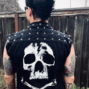 May include: Black denim vest with silver studs, a white skull with a lightning bolt design, and crossed bones on the back.