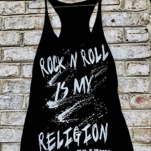 May include: Black tank top with white text that reads "Rock n Roll is my Religion" and "Rock n Horror" in smaller text at the bottom.