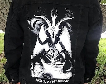 May include: Black denim jacket with a white graphic print of a goat-like figure with horns and wings. The text "Rock N Horror" is printed below the graphic.