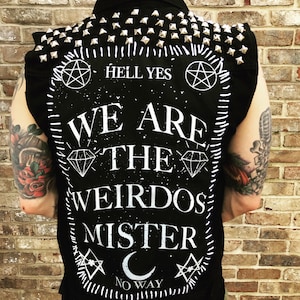May include: Black sleeveless denim vest with silver studs, white stitching, and white text that reads "Hell Yes", "We Are The Weirdos Mister", and "No Way".