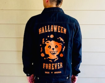 May include: Black denim jacket with an orange Halloween-themed graphic on the back. The graphic features a smiling cat face, bats, and the words "HALLOWEEN FOREVER" in a vintage font. The jacket has a classic button-up design.