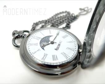 May include: A black pocket watch with a white face, Roman numerals, and a moon phase design. The watch has a matching chain and the text "MODERNTIMEZ" is visible. The watch is open, revealing the face.