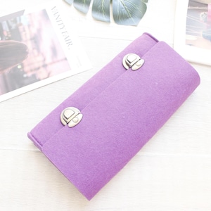 May include: A rectangular purple felt clutch bag featuring two silver-toned metal push-lock closures on the front flap. The bag has a soft, textured surface and a structured, elongated shape, providing a simple and functional design for carrying items.