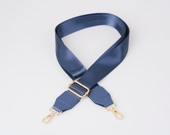 May include: A blue adjustable strap with gold hardware and two swivel clips. The strap is made of a woven fabric and has a leather-like finish.