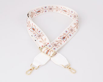 May include: White fabric strap with gold hardware and a floral pattern in shades of brown, blue, and red.