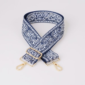 May include: A blue and white paisley patterned adjustable strap with gold metal hardware. The strap is designed to be used as a replacement strap for bags.