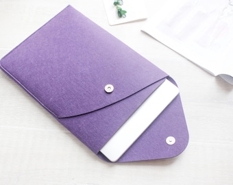 Könnte beinhalten: Eine violette Laptoptasche aus Filz mit einem weißen Laptop im Inneren. Die Tasche hat eine Klappe, die mit einem Knopf verschlossen wird.