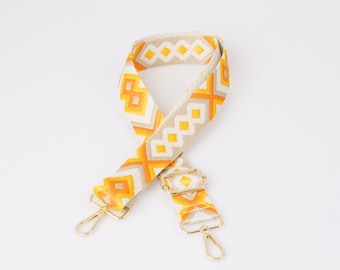 May include: A beige and orange patterned fabric strap with gold metal clasps. The strap is designed for a bag or purse.