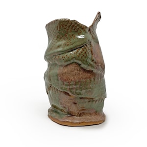 May include: Handmade ceramic vase with a unique, textured design. The vase features a blend of earthy tones, including shades of green and brown. The surface has a layered appearance with a rough, organic texture, and a small spout.