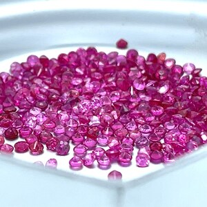 May include: A close-up view of a pile of loose pink gemstones. The gemstones are round and have a shiny, polished finish.