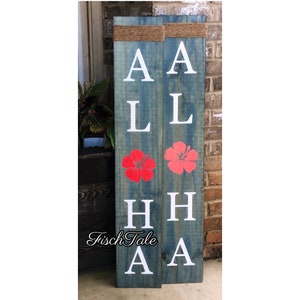May include: A wooden sign with the word "Aloha" spelled out in white letters. The sign is painted blue and has two red hibiscus flowers on it.