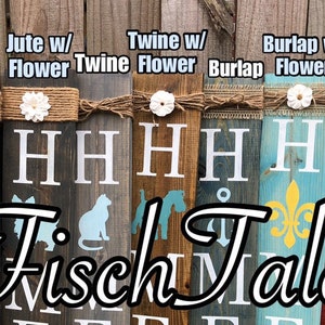 Op de afbeelding: Vijf houten borden met de tekst "Fisch Tales" in zwarte letters. Elk bord heeft een ander ontwerp en is versierd met een ander type touw: jute, touw, jute en wit touw. De borden zijn allemaal in verschillende kleuren geverfd, waaronder bruin, blauw, rood en geel.
