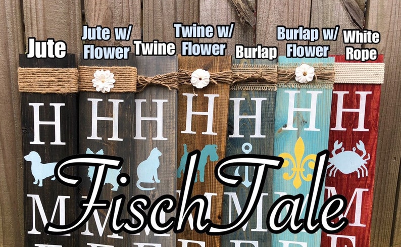 Op de afbeelding: Vijf houten borden met de tekst "Fisch Tales" in zwarte letters. Elk bord heeft een ander ontwerp en is versierd met een ander type touw: jute, touw, jute en wit touw. De borden zijn allemaal in verschillende kleuren geverfd, waaronder bruin, blauw, rood en geel.
