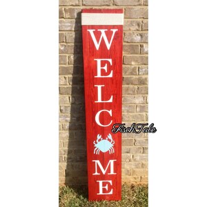 May include: Red wooden welcome sign with white letters spelling "WELCOME" and a blue crab silhouette. The sign has a white rope tied around the top.