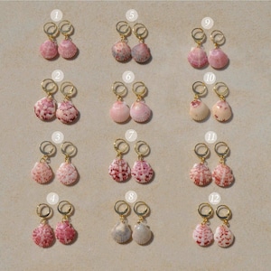 May include: A collection of twelve pairs of seashell earrings with gold-colored hoops. The shells vary in color, including pink, white, and brown. The earrings are arranged on a light beige surface, showcasing their natural beauty and unique designs.