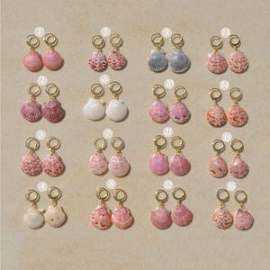 May include: Sixteen pairs of gold-toned hoop earrings, each featuring a unique natural seashell charm. The shells vary in color, including shades of pink, white, grey, and orange, and are numbered one through sixteen in a grid layout.