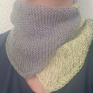 Könnte beinhalten: Ein handgestrickter Rundschal in Grau- und Hellgelbtönen. Der Schal ist aus weichem Garn gefertigt und hat ein strukturiertes Aussehen. Das Design weist einen Farbverlauf auf, der von Grau zu Gelb übergeht. Der Schal wird um den Hals getragen.